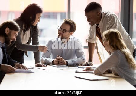 Boss sitting at desk listens creative ideas of multiethnic employees Stock Photo