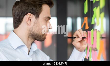 Focused businessman writing on sticky notes attached on glass wall Stock Photo