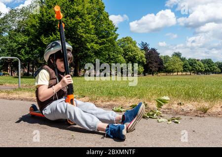 A young boy sits on his scooter on a path in the park on a sunny day Stock Photo