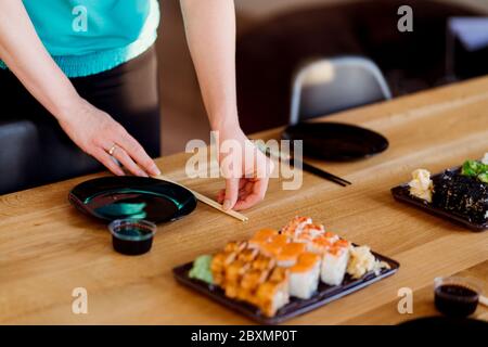Woman hands arranging the table with various sushi sets on a wood table in a sunny home Stock Photo