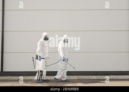 Full length wide angle view at two workers wearing protective gear and spraying chemicals outdoors during disinfection or cleaning, copy space Stock Photo