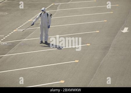 Wide angle above view at worker wearing protective gear spraying chemicals in street outdoors during disinfection or cleaning, copy space Stock Photo