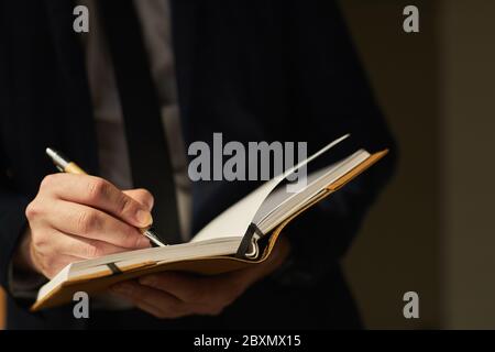 Close up of successful unrecognizable businessman writing in notebook while standing in shadow, copy space Stock Photo