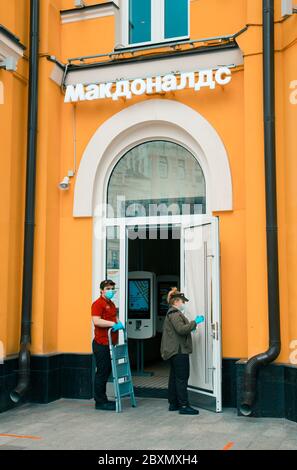 McDonald's restaurant is preparing to open during the end of the coronavirus pandemic. Employees in protective masks and gloves hang ads. Moscow, Russ Stock Photo