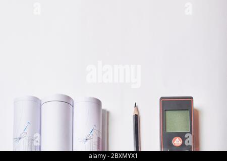 Laser meter, pencil and rolled drawings at blank white background with copy space. Stock Photo