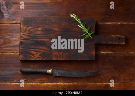 Top view cutting board on wooden background with a sprig of rosemary and a vintage knife. Flat lay copy space. Stock Photo