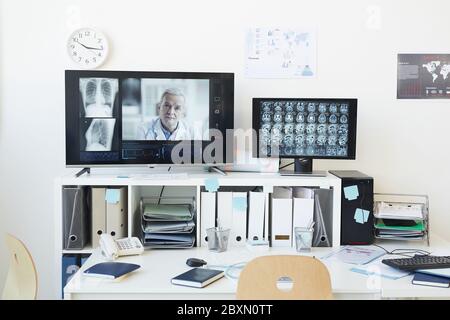 Background image of modern computer equipment for telemedicine and online consultation in clinic, focus on digital screen with CT scans and mature doc Stock Photo