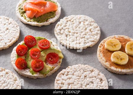 Puffed rice cakes with guacamole salmon,tomato and avocado, and banana with peanut butter on gray stone background Stock Photo