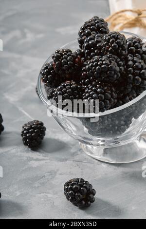 A small glass cup filled with blackberries. Close-up, ripe blackberry berries on a gray background Delivery of products, copies of space, photos for Stock Photo