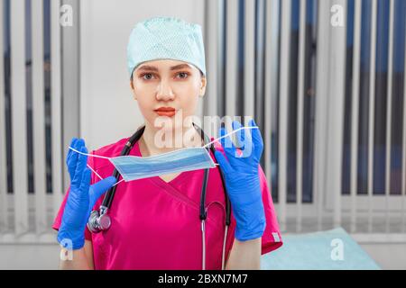 Female doctor takes off mask, victory over virus. The concept of victory over the epidemic, biological, viral. copy space, medicine, saving lives Stock Photo