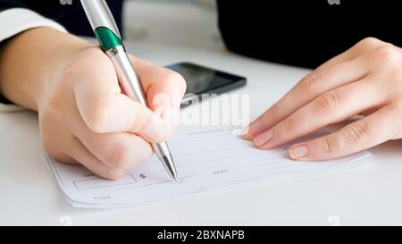 Closeup image of woman writing signature on banking cheque Stock Photo