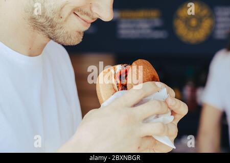 Close-up of man holds and bites hamburger, eating fast food, unhealthy food concept, toned Stock Photo