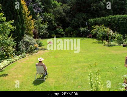 At one with nature: A lone man in a deckchair relaxes in his verdant garden Stock Photo