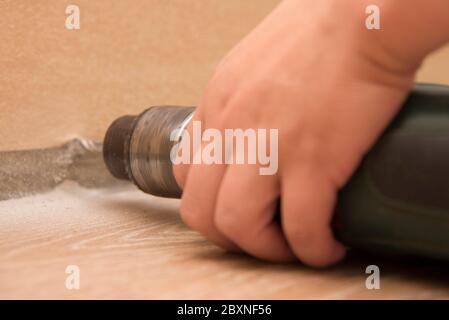 The hand holds the drill near the wall, close-up, the theme of repair work and building Stock Photo