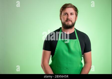 Supermarket employee with green apron and black t-shirt, isolated on green background Stock Photo