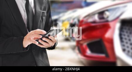 Businessman using smartphone on blurred background of new car displayed in showroom dealer with copy space. Stock Photo