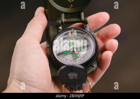 Modern navigation metal tourist compass in hand on a dark blurry background. travel or search concept Stock Photo