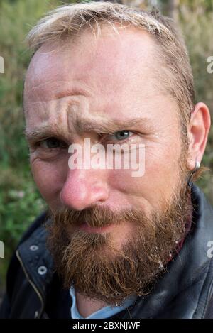 Portrait of a biker with a wet beard and an earring in a leather jacket outdoors Stock Photo