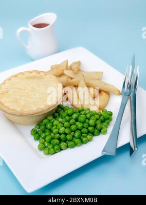 An Australian meat pie served with peas and chips isolated against a blue background Stock Photo