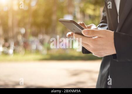 Closeup image of man holding and using mobile phone on bokeh background outdoor. Stock Photo