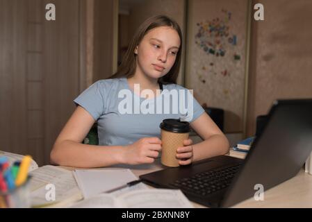 Teen girl, home lessons laptop, cup of coffee tea, watching videos, learning lessons, home education, preparing for exam institute and school Stock Photo