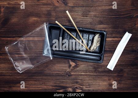 top view of a plastic tray of precooked asiatic food and chopsticks on a dark wooden table, concept of oriental fast food to take away, copy space for Stock Photo