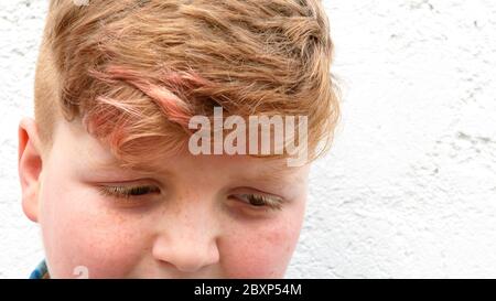 Plump red-haired boy is smiling. A boy in a plaid shirt stands on a wall background and smiles. Stock Photo