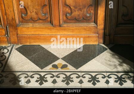 wooden door and decorated floor at the entrance of a church in Italy Stock Photo