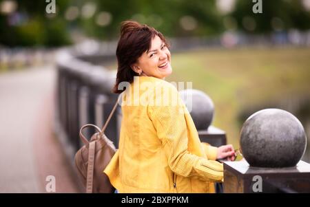 Beautiful well-groomed energetic middle-aged woman posing coquettishly while the sun while walking around the city in summer. Concept of middle-aged w Stock Photo