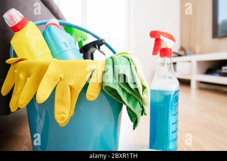 Blue bucket for cleaning with yellow gloves and a variety of detergents with rags. Room cleaning.Bucket with cleaning items on light background Stock Photo
