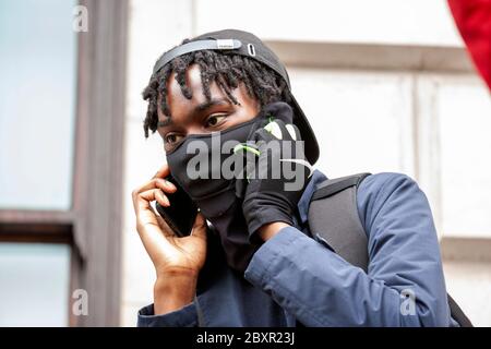Young man with short dreadlocks, wearing a face mask and using a mobile phone at the Black Lives Matter UK protest, Parliament Square, London, England Stock Photo