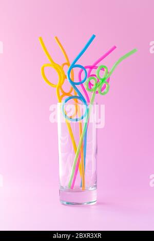 Glass with many plastic colorful cocktail straws on a pink background, fun mood concept. Abstraction, creative concise design Stock Photo