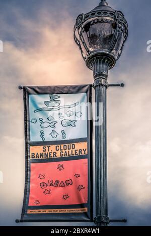 Colorful and whimsical graphic banner for the St. Cloud Banner Gallery hangs from a retro antique lamp post in the downtown district of St. Cloud, MN Stock Photo