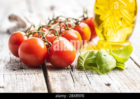 Red cherry tomatoes and basil leaves on wooden table. Stock Photo