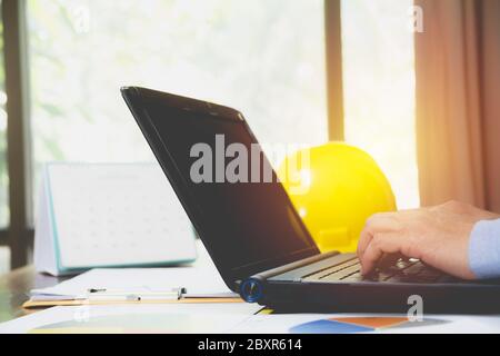 Architect engineer using laptop for working with yellow helmet on desk. Stock Photo