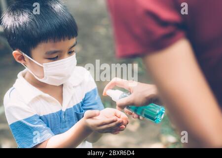 Mother take care son with face mask and sanitizer for protection disease flu or covid-19 outdoors, mom and child wearing medical mask clean hand for s Stock Photo