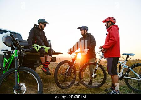 Friends Cyclists Resting near the Pickup Off Road Truck after Enduro Bike Riding in the Mountains at Warm Autumn Sunset. MTB Adventure and Car Travel Stock Photo