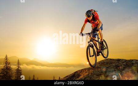 Cyclist in Red T-Shirt Riding the Bike in the Beautiful Mountains Down the Rock on the Sunrise Sky Background. Extreme Sport and Enduro Biking Concept Stock Photo
