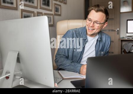 Young man working from home doing paperwork while using laptop and holding phone in his hand. Stock Photo