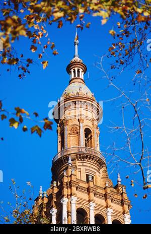 Ancient architecture tower view in Plaza de España against blue sunny clear sky framed by tree leaves. Main landmark popular place for tourists, trave Stock Photo