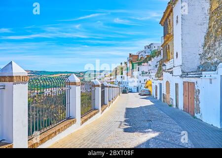 The old street runs along the steep slope of the city hill and opens the view on white living quarters and mountain landscapes in Arcos surroundings, Stock Photo