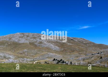 A meadow with a downed fence at the end of the meadow. In the background, mountain desolation. On the way to the mountain Bjelasnica, Bosnia and Herze Stock Photo