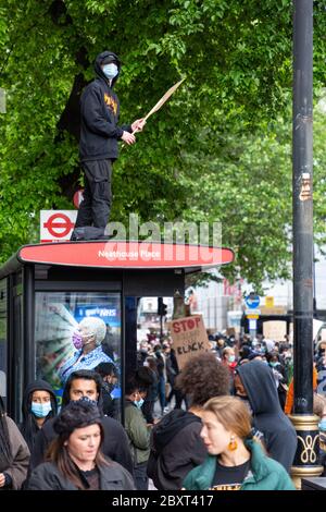 A protester stands on top of a bus stop and holds up a sign during the Black Lives Matters protest on Vauxhall Bridge Road, London, 6 June 2020 Stock Photo