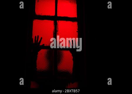 Scary sihouette of person leaning against window in dark Stock Photo