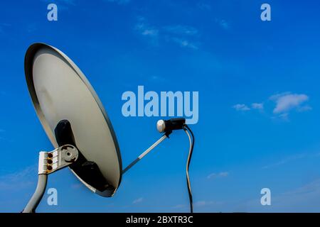 White satellite antenna with white and black cable blue sky in background Stock Photo