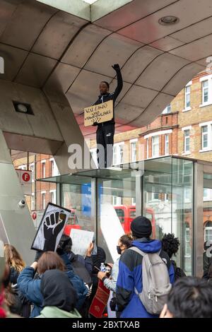 A black man stands with his fist raised on top of a bus stop at Vauxhall bus station, during Black Lives Matters protest in London, 6 June 2020 Stock Photo