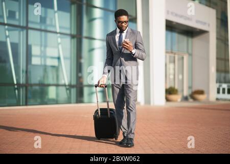 African Businessman Using Smartphone Waiting For Flight Standing At Airport Stock Photo