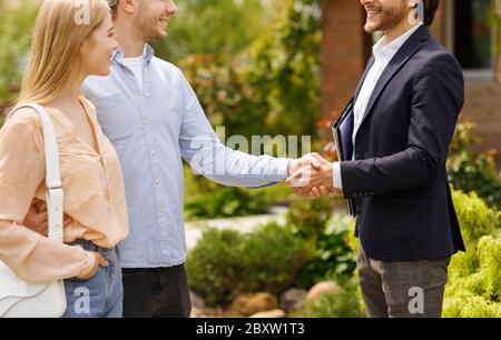 Cropped view of real estate broker shaking hands with his clients, closing house rental deal outdoors Stock Photo
