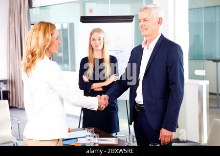 Shot of executive business people shaking hands while on business meeting. Senior businessman greetings his new colleague. Stock Photo