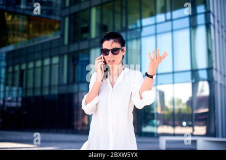 Nervous woman using mobile phone and talking with somebody while walking on the street. Stock Photo